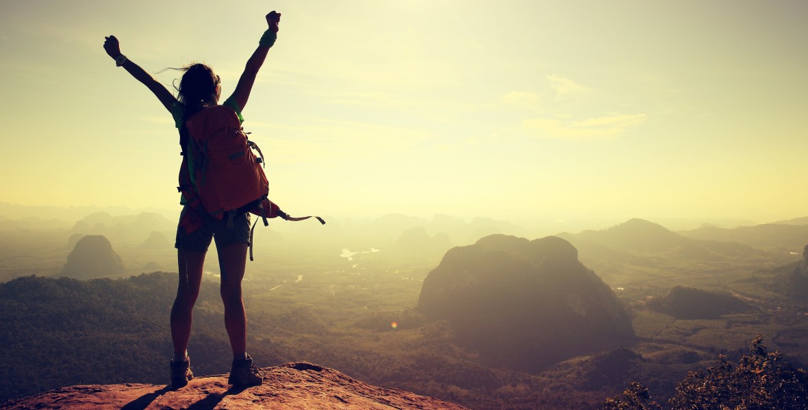 silhouette of free cheering woman hiker open arms at mountain peak